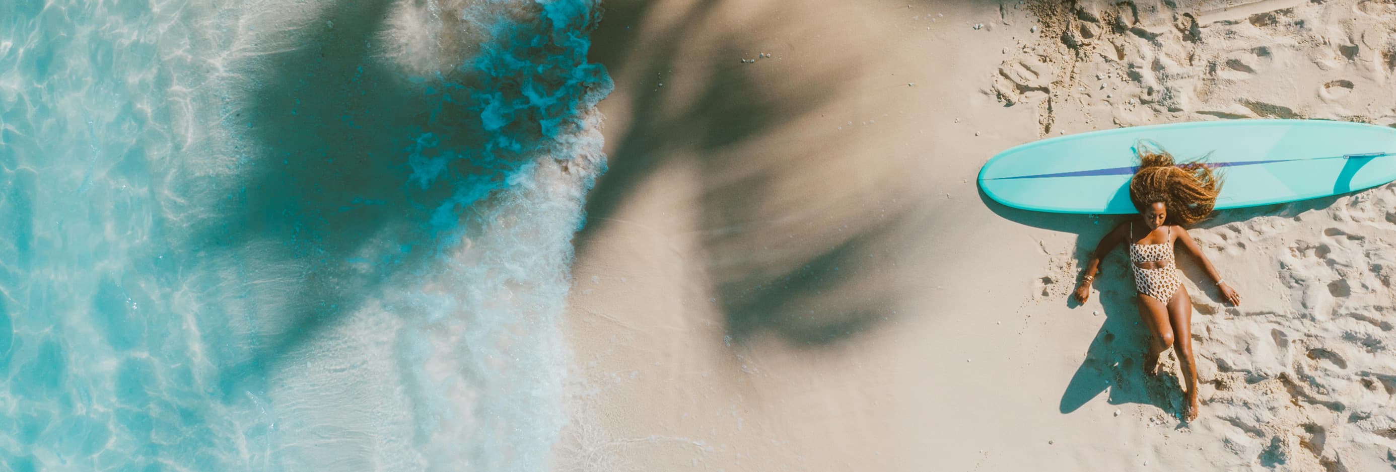 Aerial view of a surfer lying on a tropical beach beside a surfboard