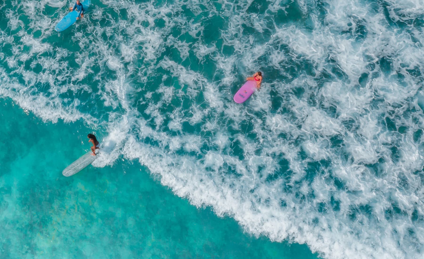 Aerial view of surfers paddling through whitewater in turquoise water off Bali